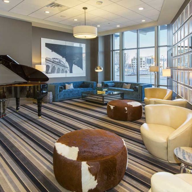 Cadence Union Station Apartments - Three Modern Lounge with Grand Piano, Striped Carpet, Seating, and Large Windows 
