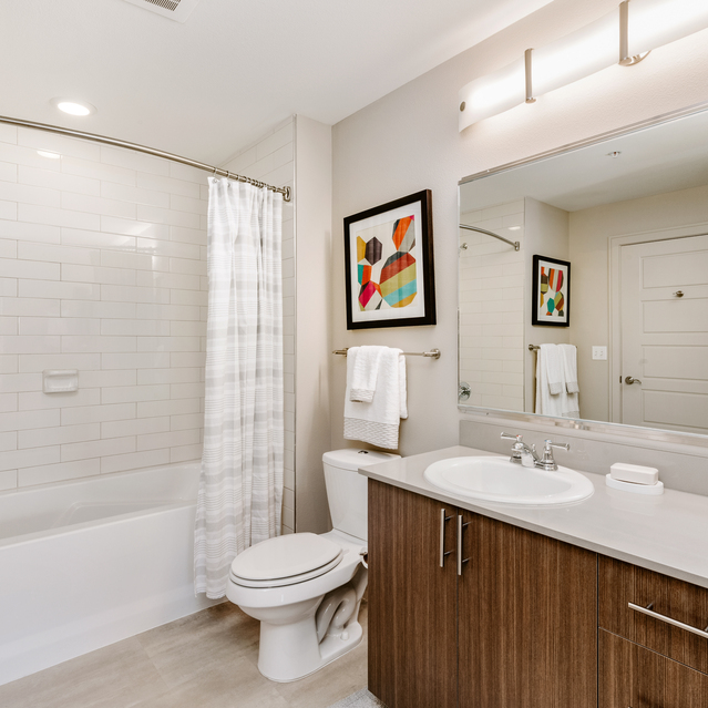 Cadence Union Station Apartments - Modern Bathroom with Wooden Vanity, White Countertop, Bathtub, and Colorful Wall Art 