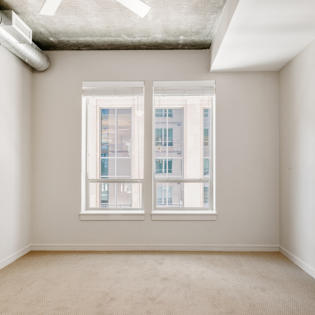 Cadence Union Station Apartments - Empty Room with White Walls, Beige Carpet, and Large Windows Showing Building View