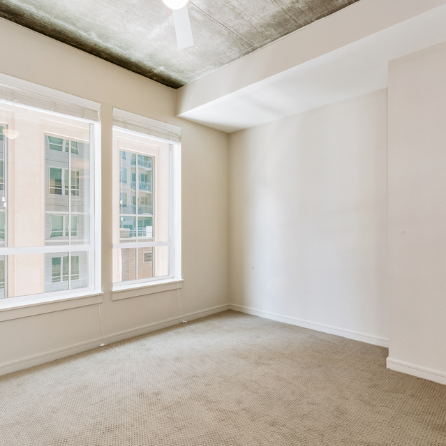 Cadence Union Station Apartments - Empty Room with White Walls, Beige Carpet, and Large Windows Showing Building View