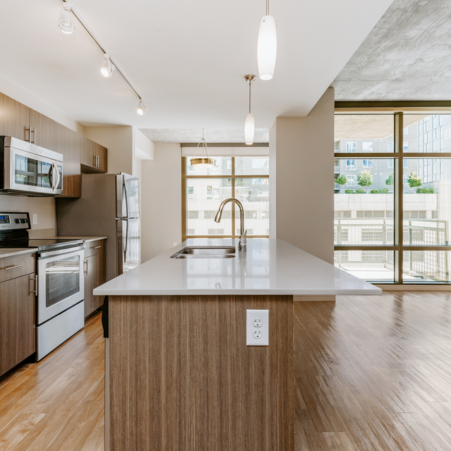Modern Kitchen with Wooden Cabinets, Stainless Steel Appliances, White Island Countertop, and Large Windows with Natural Light 